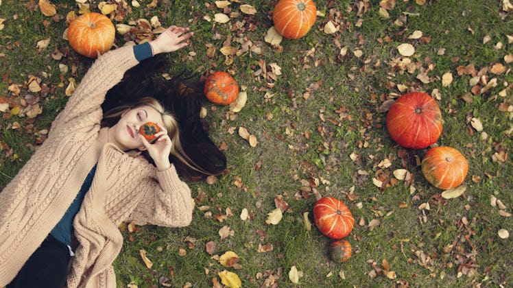 A beautiful woman is lying on the grass. Top view. She lies near the pumpkins. She holds a small dec...