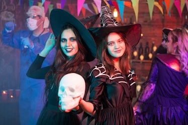 Sisters dressed up like witches at a halloween party holding a skull. Witches gathering. Halloween c...