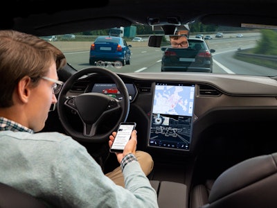 A man reads news online in a smartphone while his car is driven by an autopilot. Self driving vehicl...
