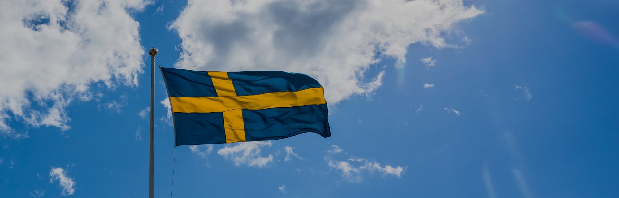 Swedish Flag on blue sky white clouds. Swedish Flag Day concept in Sun rays . Sveriges nationaldag. ...