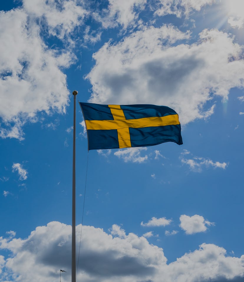Swedish Flag on blue sky white clouds. Swedish Flag Day concept in Sun rays . Sveriges nationaldag. ...