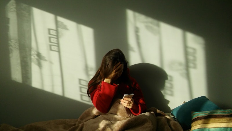 Sad woman making a phone call on the bed. Depressed, evastated woman sitting in bed and holding the ...
