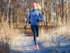 Young slim girl running in the park in early winter. Attractive woman jogging on snowy trail
