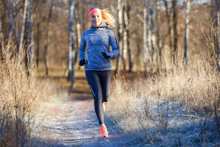 Young slim girl running in the park in early winter. Attractive woman jogging on snowy trail