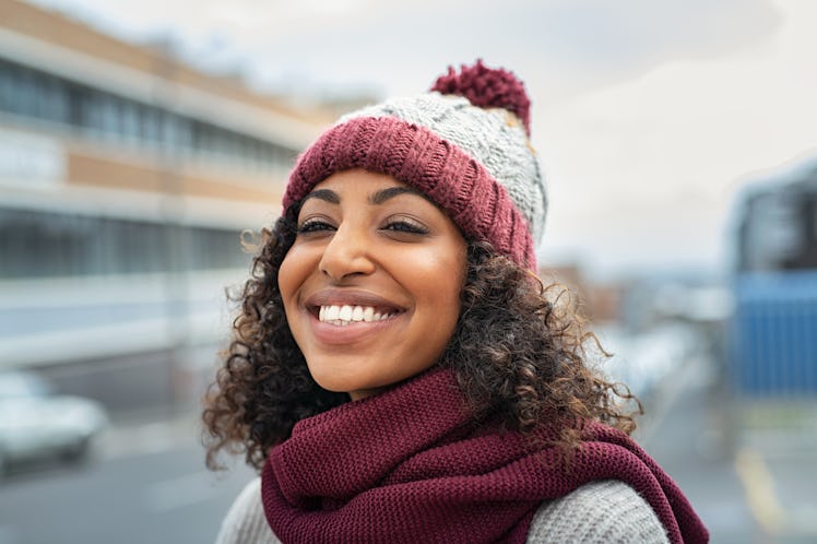 Closeup face of young happy woman enjoy winter, wearing scarf and woolen cap. Smiling black girl loo...