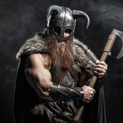 Medieval warrior berserk Viking with axes attacks enemy. Concept historical photo of Scandinavian go...