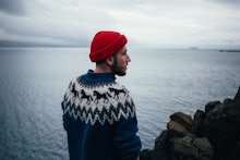 Young handsome man with beard wears traditional authentic blue wool knitted sweater with ornaments a...