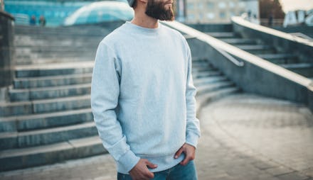 City portrait of handsome hipster guy with beard wearing gray blank hoodie or hoody and hat with spa...
