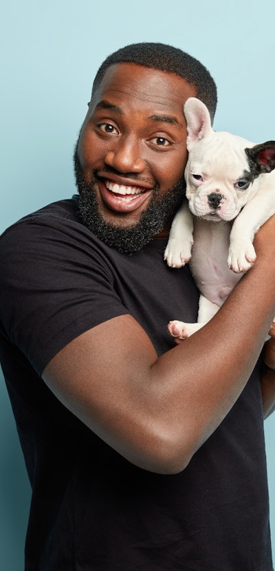 Happy satisfied smiling dark skinned man carries small pet of french bulldog breed, spend leisure ti...