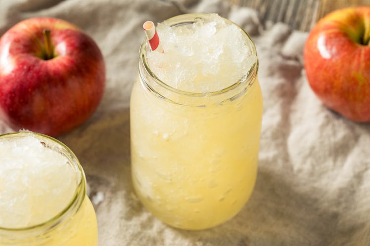An apple cider slushie sits in a mason jar on a tablecloth with crisp apples.