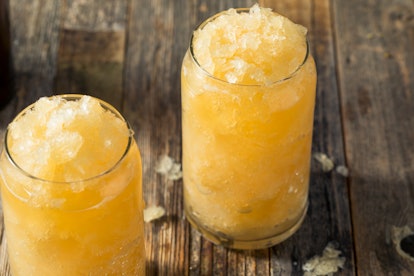 Two apple cider slushies sit in large glasses on a wooden picnic table.