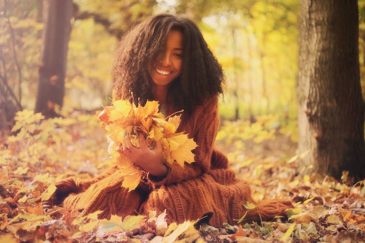 Young black woman with autumn leaves in hands relaxing in the autumn forest on a sunny day. 