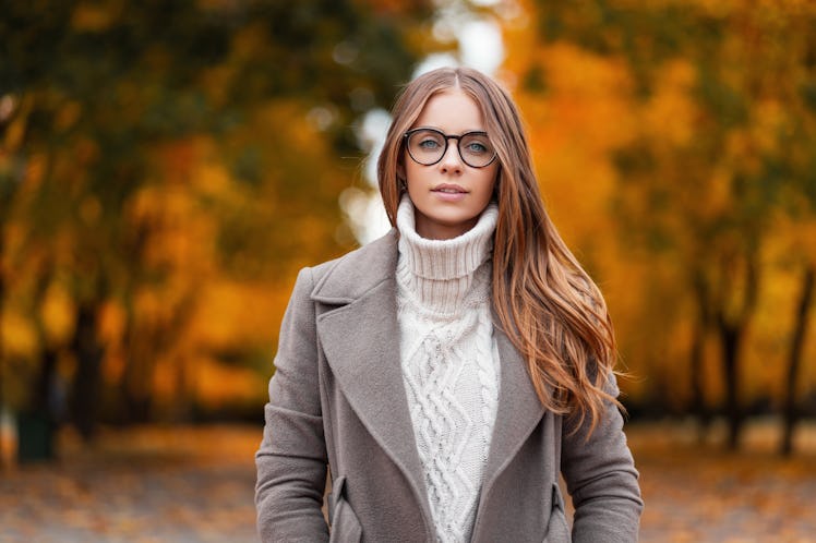 Autumn portrait of an attractive young woman in stylish glasses in a knitted fashionable white sweat...