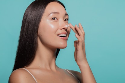 Close up of female model applying moisturizer cream to her nose. Woman applying moisturizer cream on...