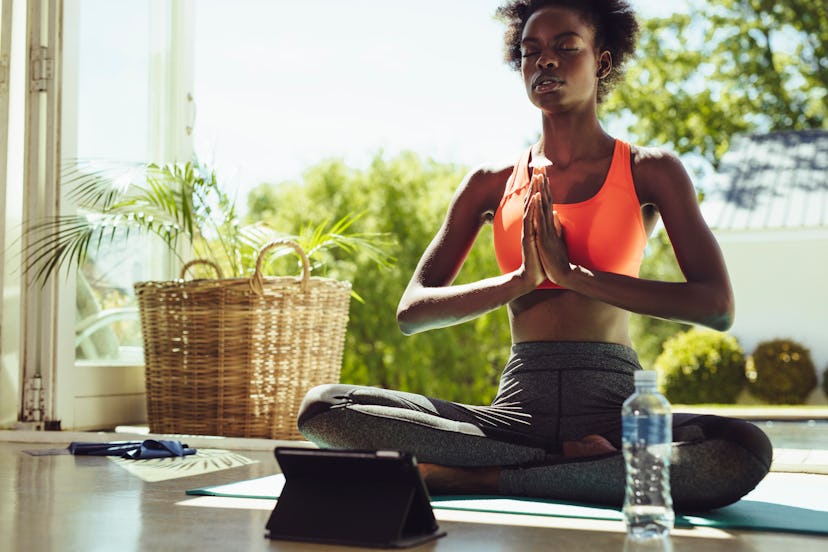 Healthy woman sitting on yoga meditation at home with a digital tablet in front. Fitness woman in sp...