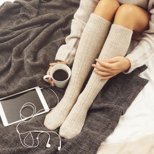 Woman in warm woolen stockings is drinking hot coffee at cold winter day