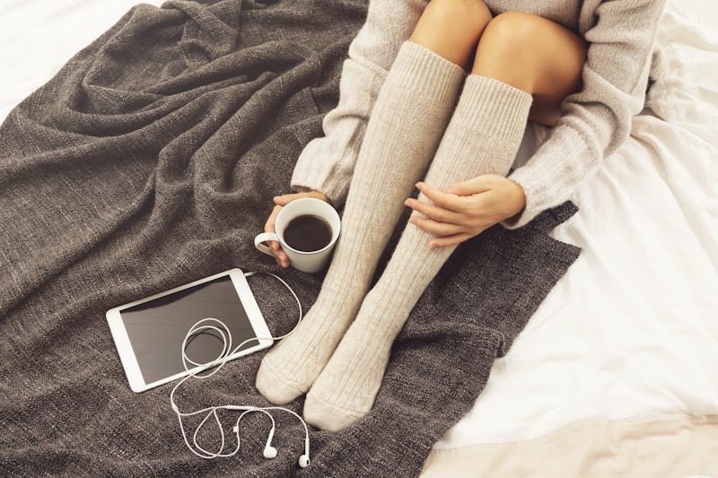 Woman in warm woolen stockings is drinking hot coffee at cold winter day