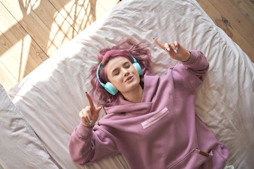 Woman listening to Alexa playlist via headphones on her bed.