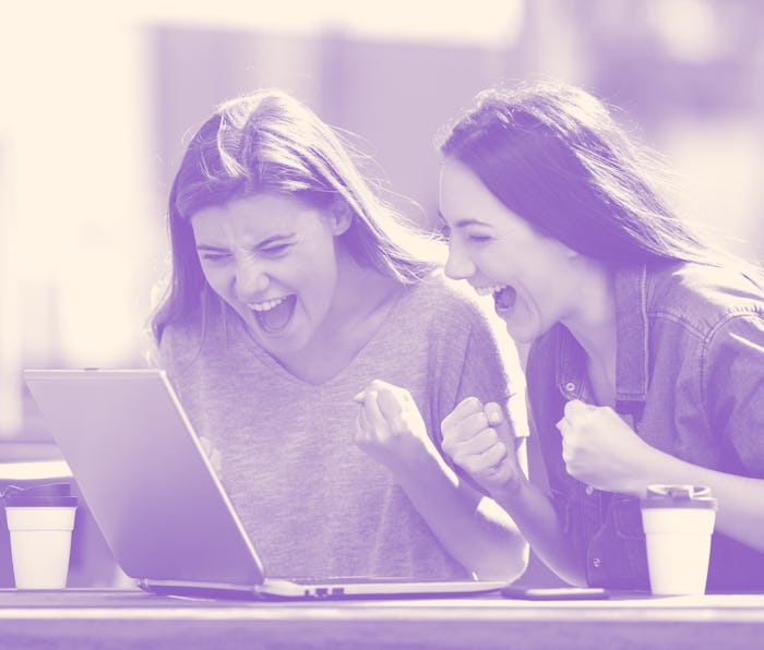 Two excited women checking laptop online content sitting in a park