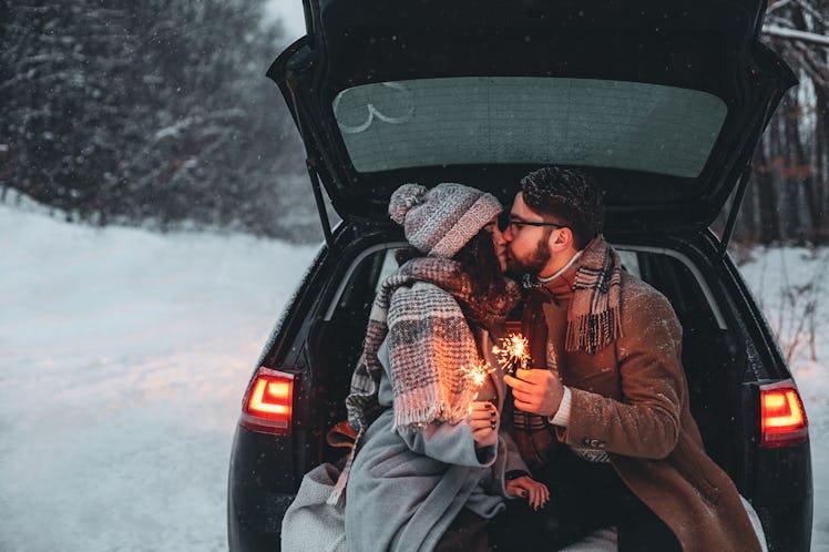 A couple sitting at the back of a car and having picnic in a snow forest. Winter romantic atmosphere...