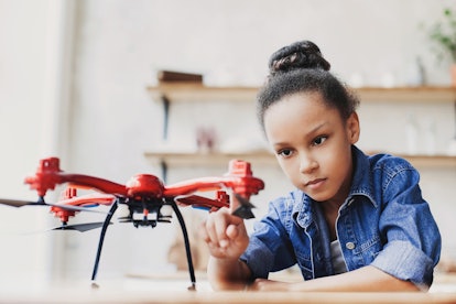 Young cute girl holding quadcopter. Child playing with drone at home. Education, home studying, chil...