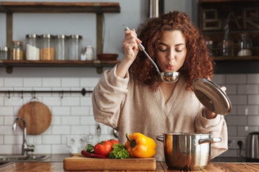 Photo of pretty caucasian woman holding cooking ladle spoon while eating soup with fresh vegetables ...