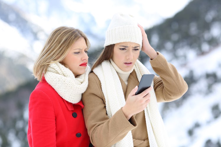 Two confused friends with a smart phone in winter on holidays in a snowy mountain