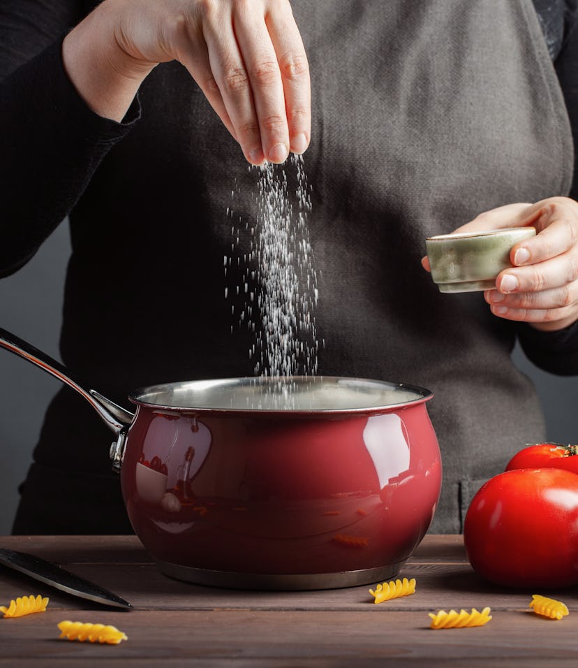The chef preparations spaghetti and pasta, salt water, against a dark background, the concept of coo...