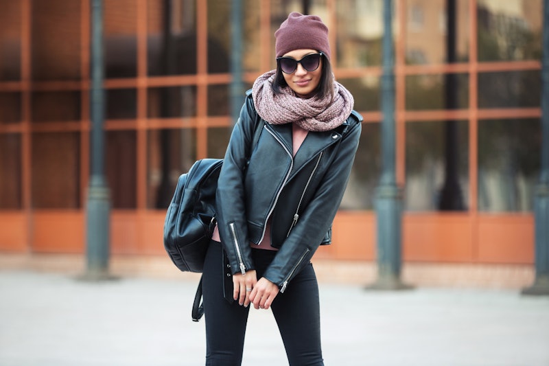Young fashion woman with backpack walking on city street Stylish female model in leather jacket bean...
