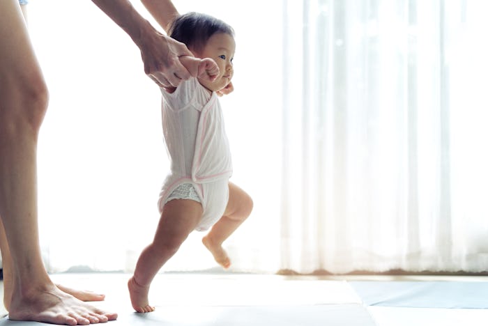 Asian baby taking first steps walk forward on the soft mat. Happy little baby learning to walk with ...