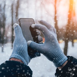 Man using smartphone in winter with gloves for touch screens. Backgound