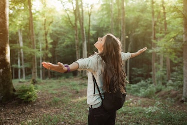 Young woman emgracing the sun and nature with backpack in the forest on sunset light in the autumn s...