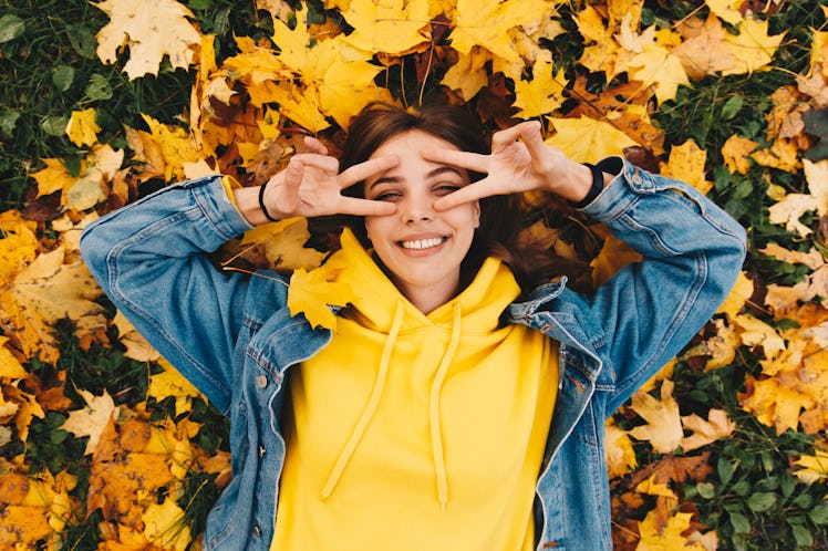 Autumn walk. Woman portrait. Happy girl in yellow hoodie and jean jacket is smiling and gesturing wh...