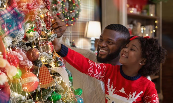 Christmas fun with daddy. Little black girl helping father to decorate family Xmas tree, enjoying wi...