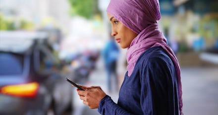 Black female in her 20s wearing hijab texting on cellphone on urban street