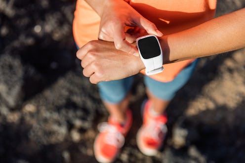 Trail runner athlete using her smart watch app to monitor fitness progress or heart rate during run ...