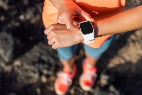 Trail runner athlete using her smart watch app to monitor fitness progress or heart rate during run ...