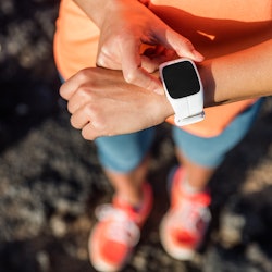 Trail runner athlete using her smart watch app to monitor fitness progress or heart rate during run ...