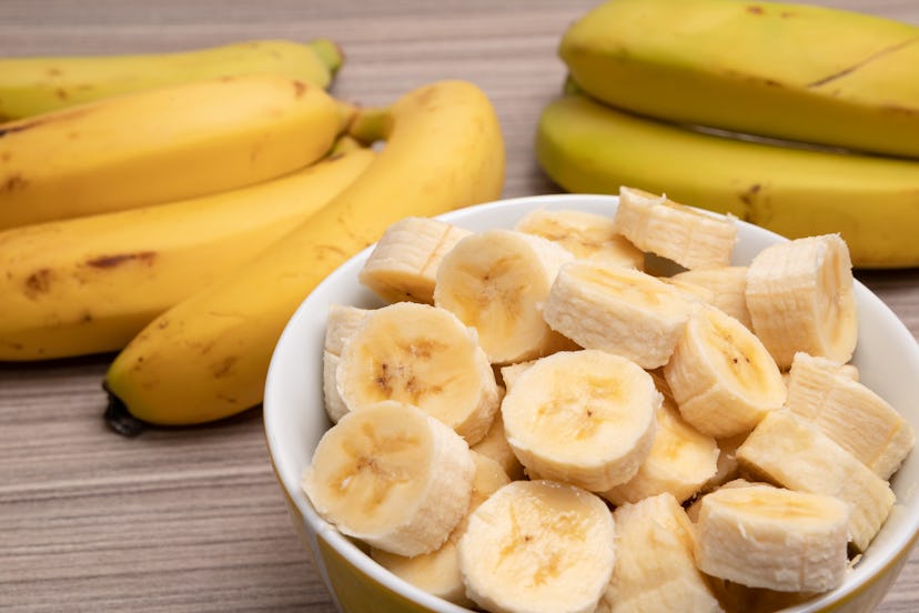 Sliced ​​bananas and a bunch of bananas in the background on a table.