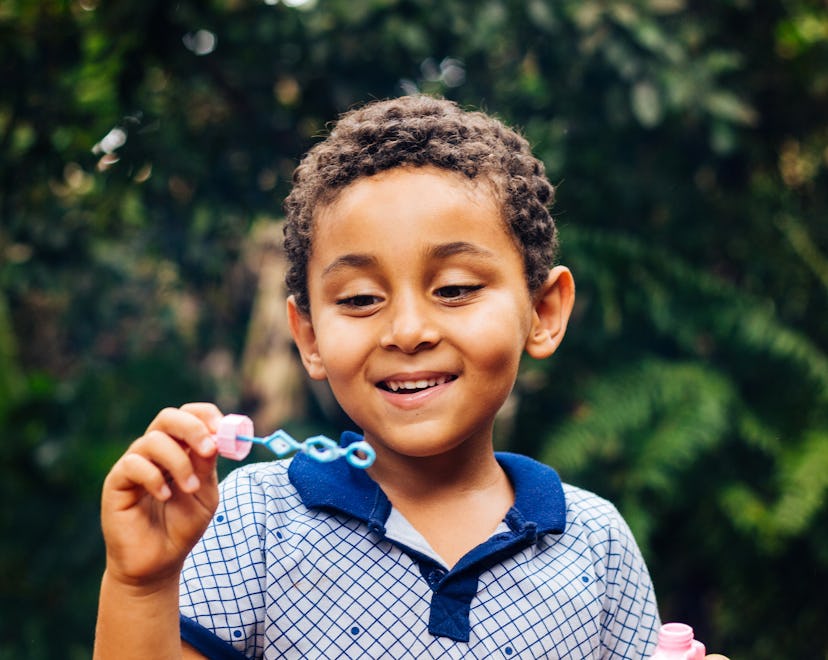 
Smiling Brazilian child playing with soap bubbles in the home garden. Boy happy. Lifestyle. Childre...