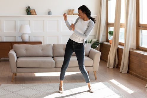 Overjoyed African American young woman dancing in modern light living room alone, happy biracial mil...