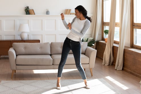 Overjoyed African American young woman dancing in modern light living room alone, happy biracial mil...