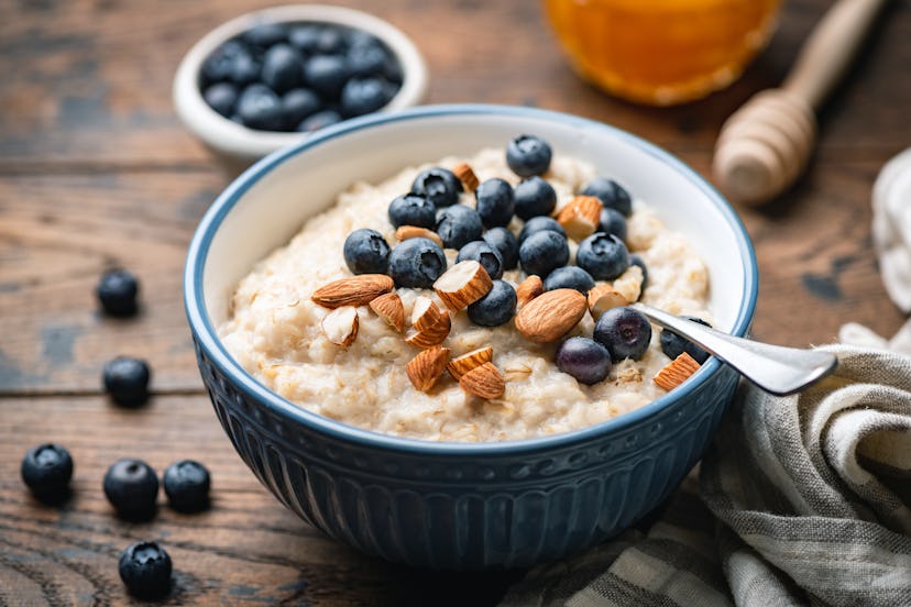 Oatmeal porridge with blueberries, almonds in bowl on wooden table background. Healthy breakfast foo...