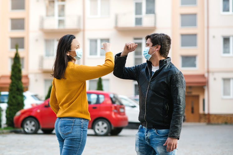 Friends greetings with elbows outdoors. Woman and man wearing face mask outdoors. Friends shaking el...