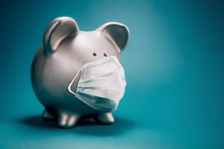 Close up of piggy bank, wearing protective face mask, isolated on blue background. Money saving conc...
