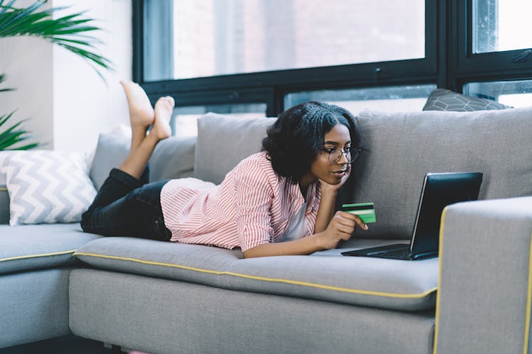 African American young woman doing online payment of tickets by credit card on laptop computer lying...