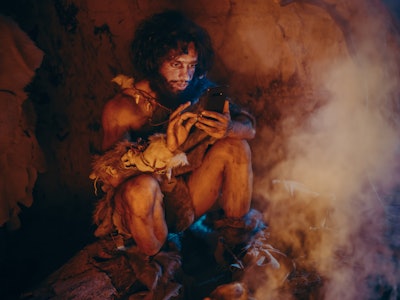 Tribe of Prehistoric, Primitive Hunter Gatherer Wearing Animal Skin Uses Smartphone in a Cave at Nig...