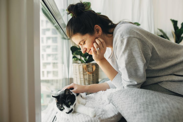 Hipster girl playing with cute cat, sitting together at home during coronavirus quarantine. Stay hom...