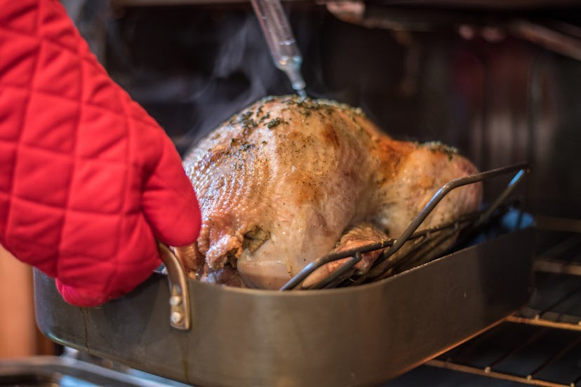 Christmas turkey being basted in the oven with red oven mitts