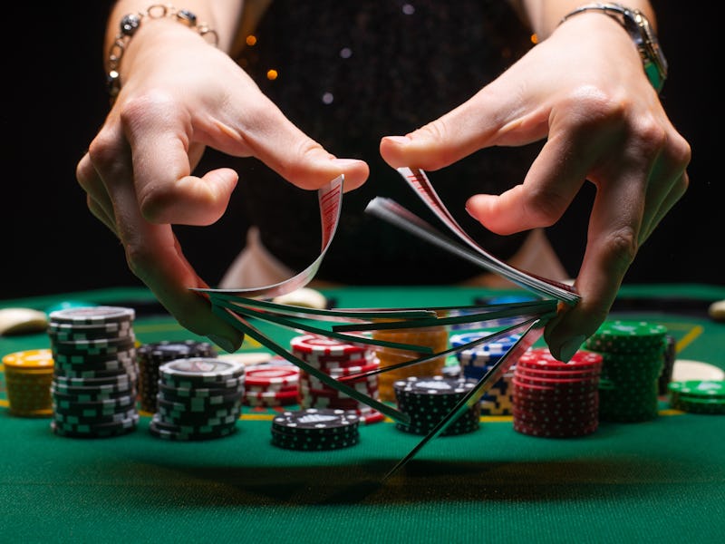 Girl dealer or croupier shuffles poker cards in a casino on the background of a table, chips,. Conce...